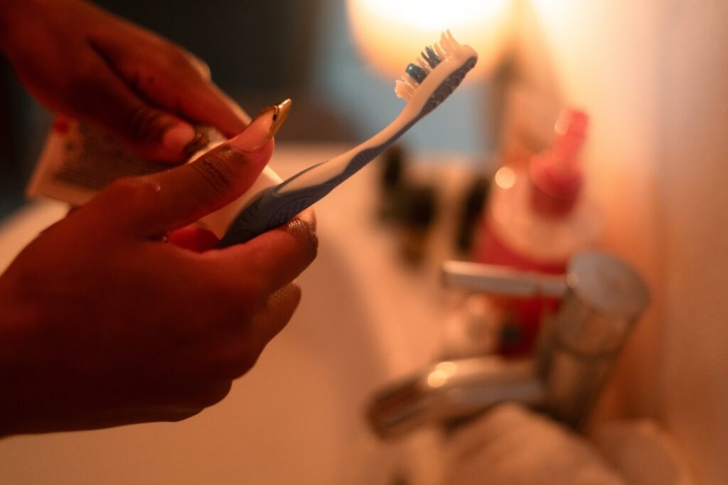 A person compares an electric toothbrush and a soft-bristled manual toothbrush beside a bathroom sink.